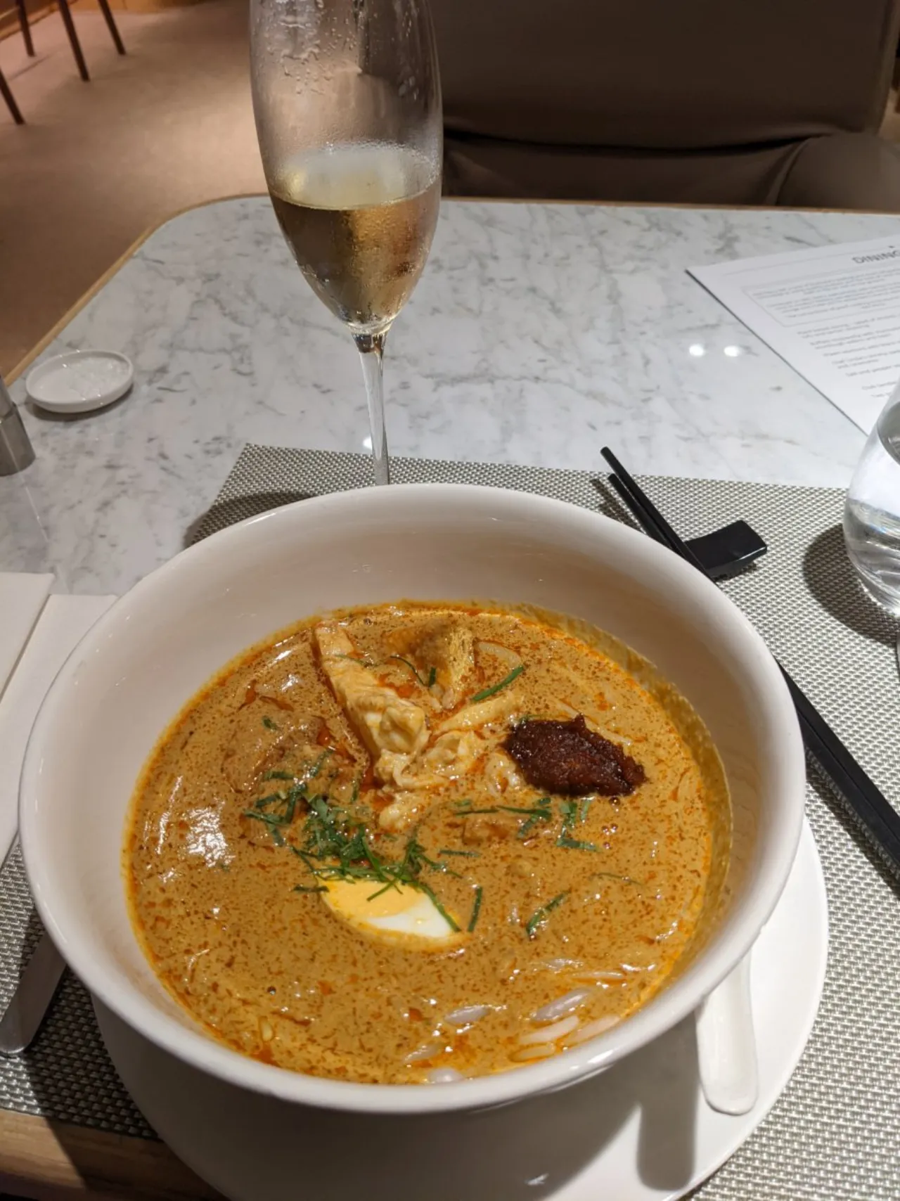 The signature laksa served with a glass of Champagne in the Qantas Singapore First Lounge
